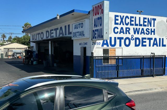 A green car drives past a blue and white building labeled "Excellent Car Wash & Auto Detail."