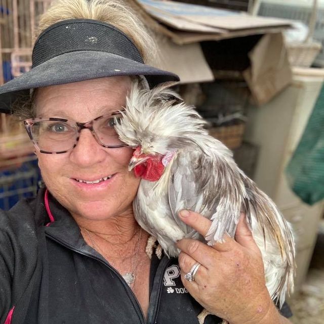 A woman holds a rooster close to her face.