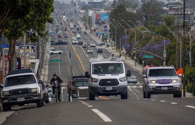 A person on a bike rides in the street alongside trucks.