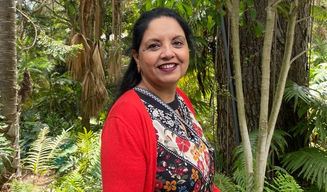 A woman smiles while standing in front of a forest.