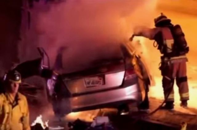 Two firefighters work to put out a car that is on fire.