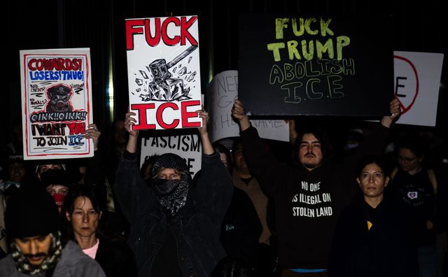 People at night hold signs saying slogans like "Fuck Ice" and "Fuck Trump Abolish Ice."