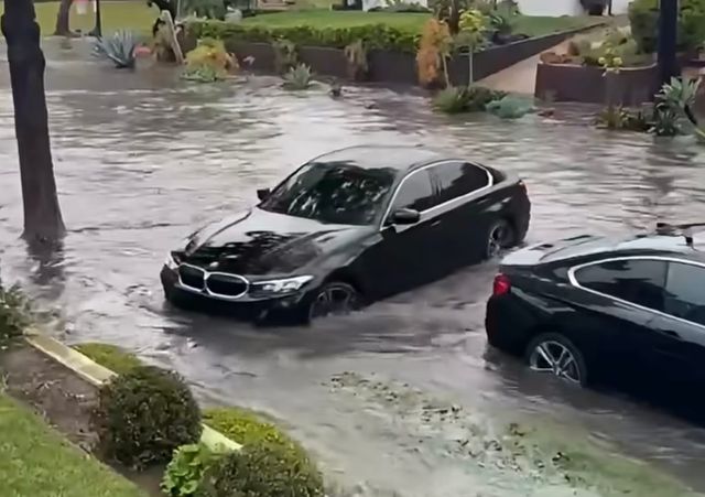 Two black cars sit in a flooded street.