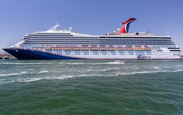 A man rides a jet ski in front of a large blue and white cruise ship.