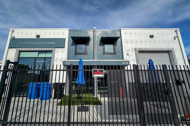 A building labeled "Youth Navigation Center" sits behind a tall black fence holding a prominent "No Trespassing" sign.