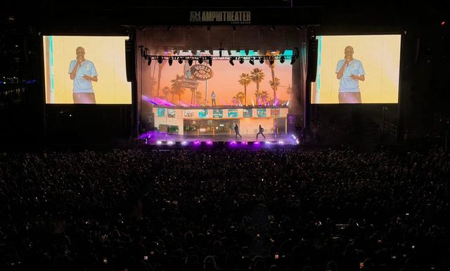 A man's on-stage performance at night is broadcast on two giant screens on either side of the stage.