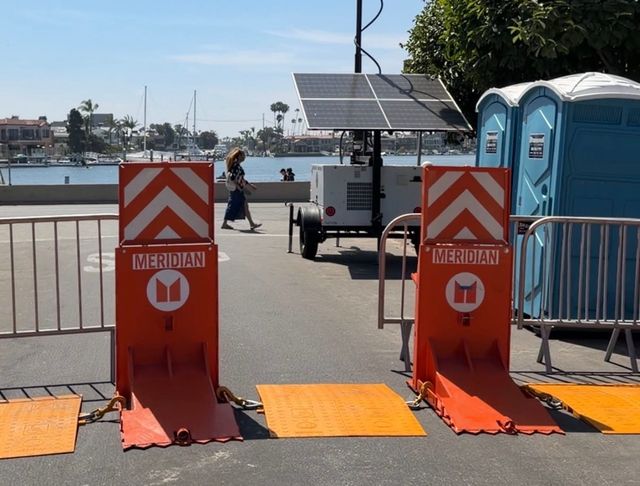 Two large orange barriers sit in the middle of the street next to two blue portable toilets and a solar-powered generator.