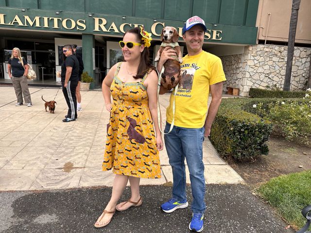 A woman wearing a yellow dress covered in little brown dogs stands next to a man wearing a yellow t-shirt and holding a small brown dog.