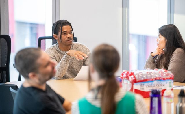 People sit around a table that has a lot of bottles of water and talk.