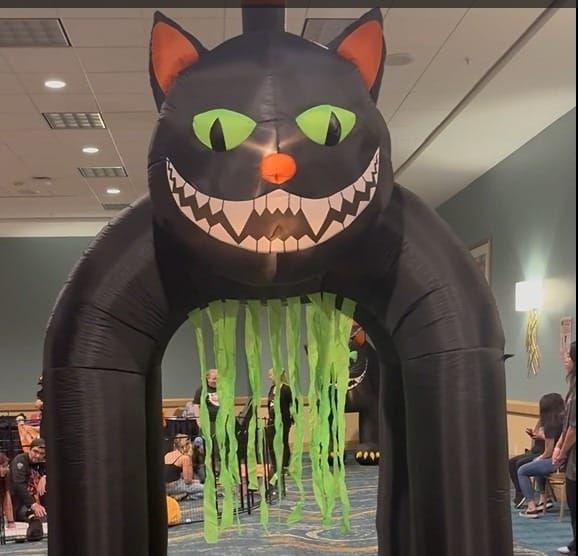 Kids sit around a giant inflatable black cat in a large room.