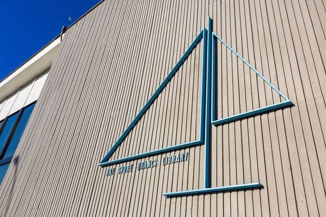 A wooden wall outside with the outline of a sailboat and the words "Bay Shore Branch Library."