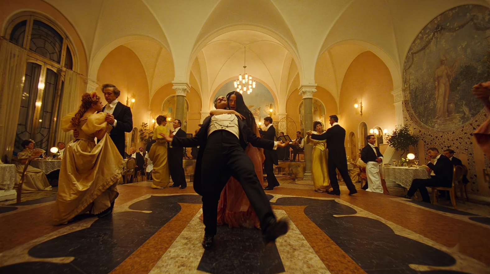 Couples in formal dress dance in a ballroom. Front and center are a couple who aren't dancing in a tranditional way; with her right arm executing a chokehold, she appears to be frog-walking her partner.