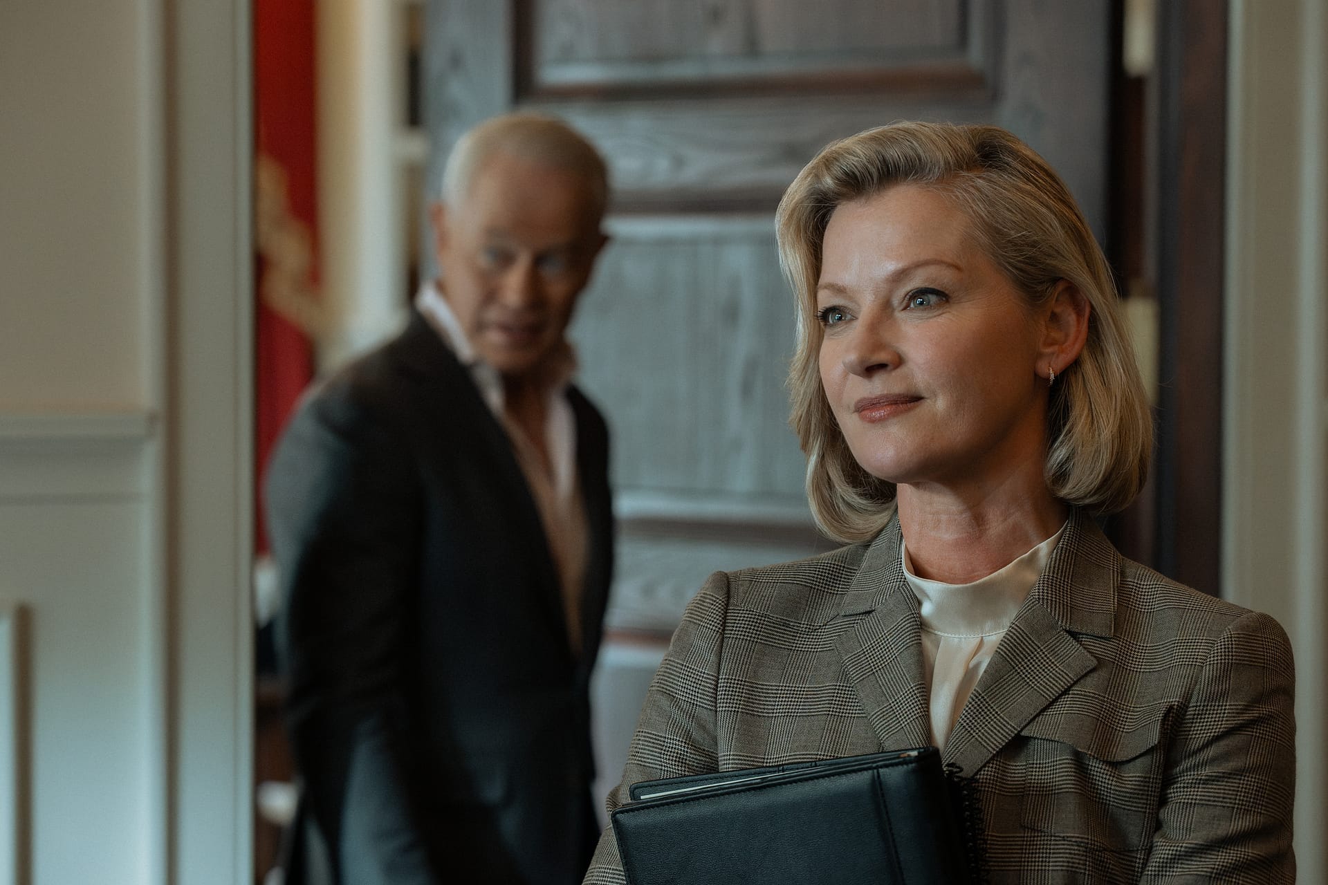 Gretchen Mol mit Mappe im Vordergrund, Neal McDonough im Hintergrund, Szene aus "Tulsa King"