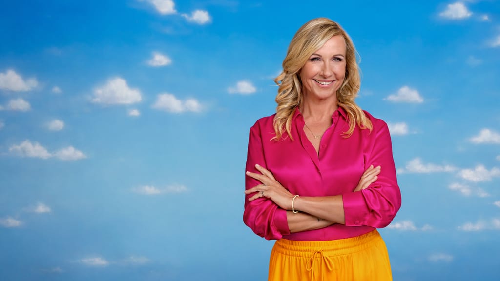 Andrea Kiewel in pinkfarbener Bluse vor Wolkenhimmel