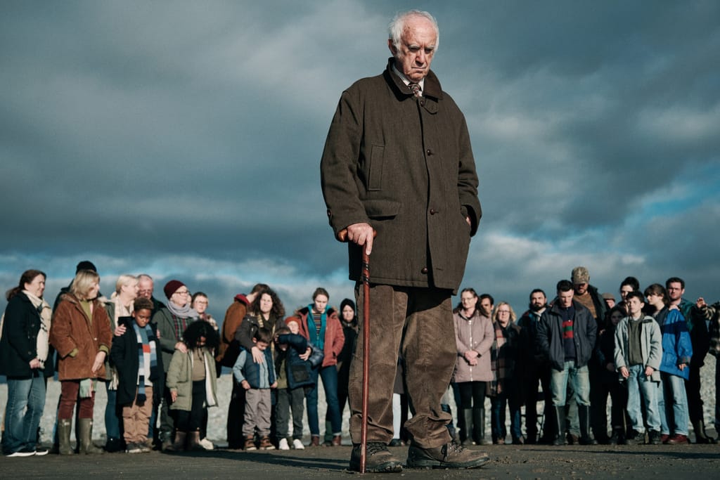 Jonathan Pryce steht mit Stock vor einer Menschenmenge unter dunklem Himmel