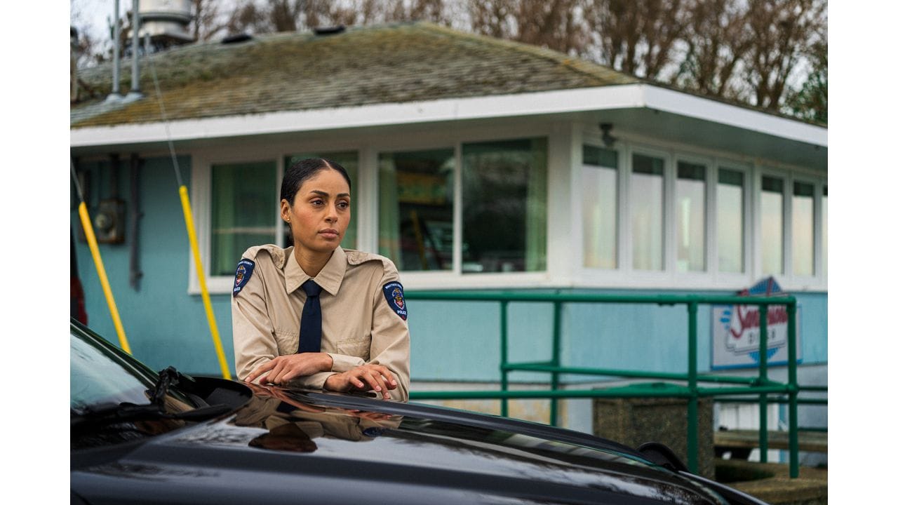 Clark Backo in Uniform an einem Auto vor einem hellblauen Haus, Szene aus "Yaga"