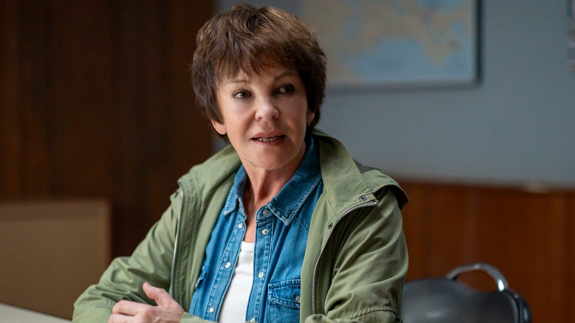 Katrin Sass in grüner Jacke an einem Schreibtisch