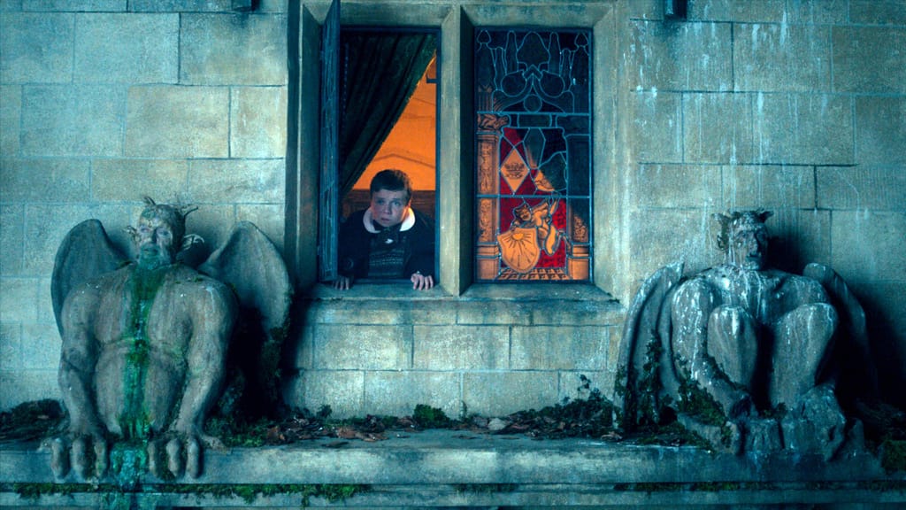 Zwei steinerne Wasserspeier vor einem Schlossfenster, aus dem Lenny Rush als Val schaut, Szene aus "The Reluctant Vampire"