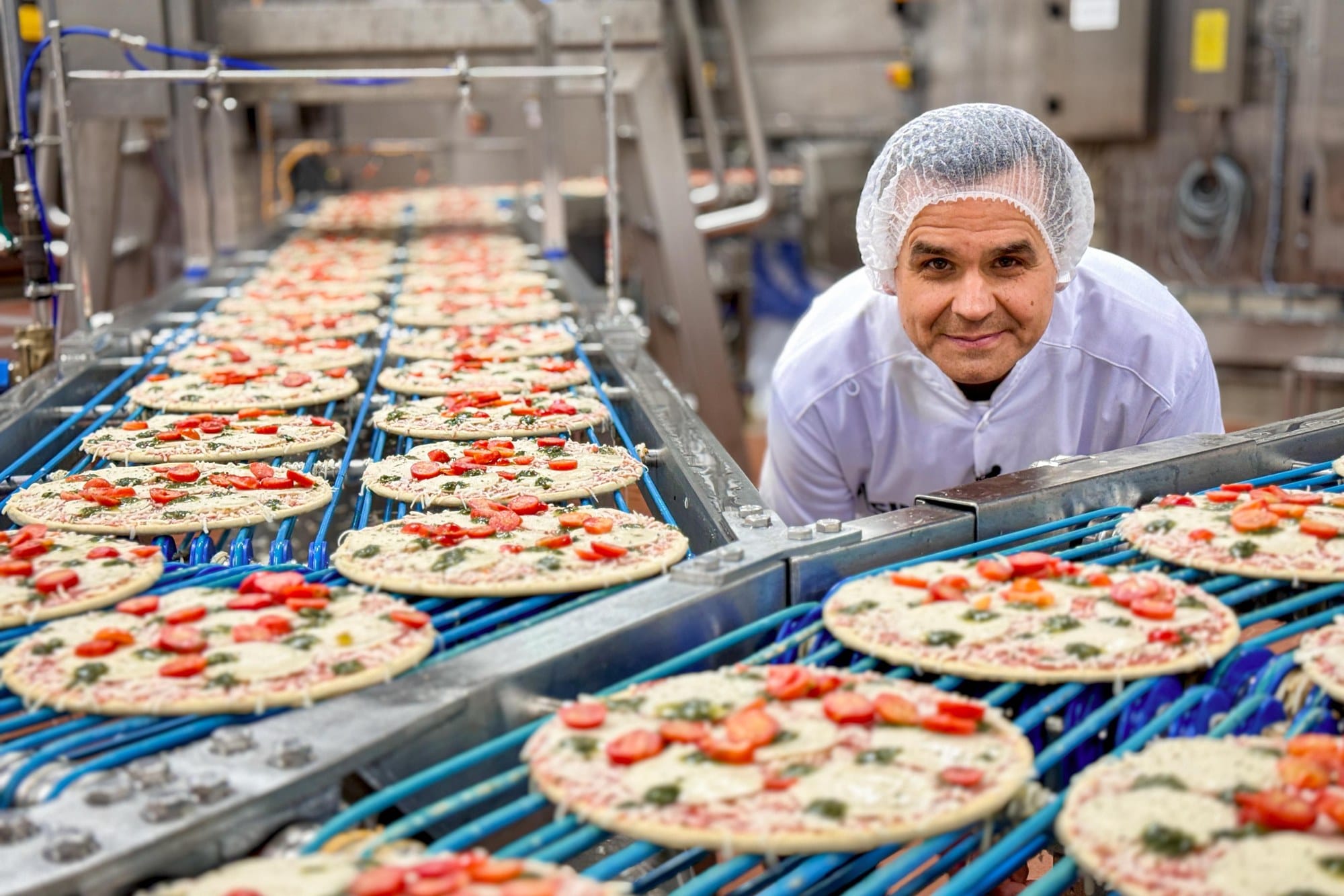 Stefan Uhl mit Haarnetz an einem Fließband voller Pizzen