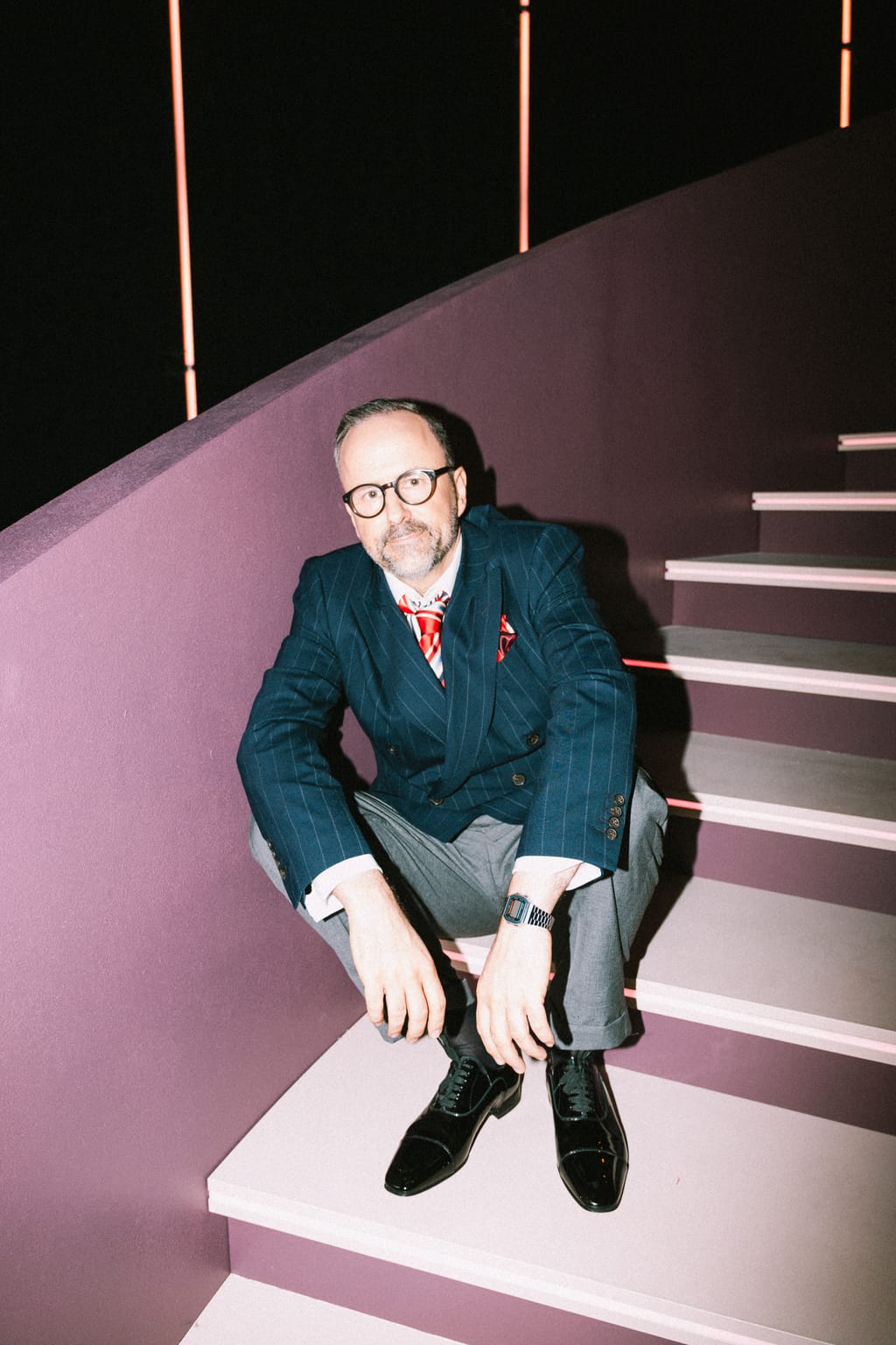 Kurt Krömer sitzt im Anzug auf einer rosa Treppe im Studio