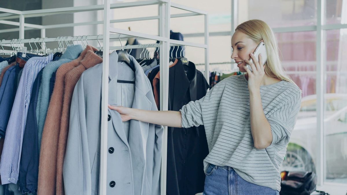 Frau telefoniert und sieht sich Mäntel an einer Kleiderstange an