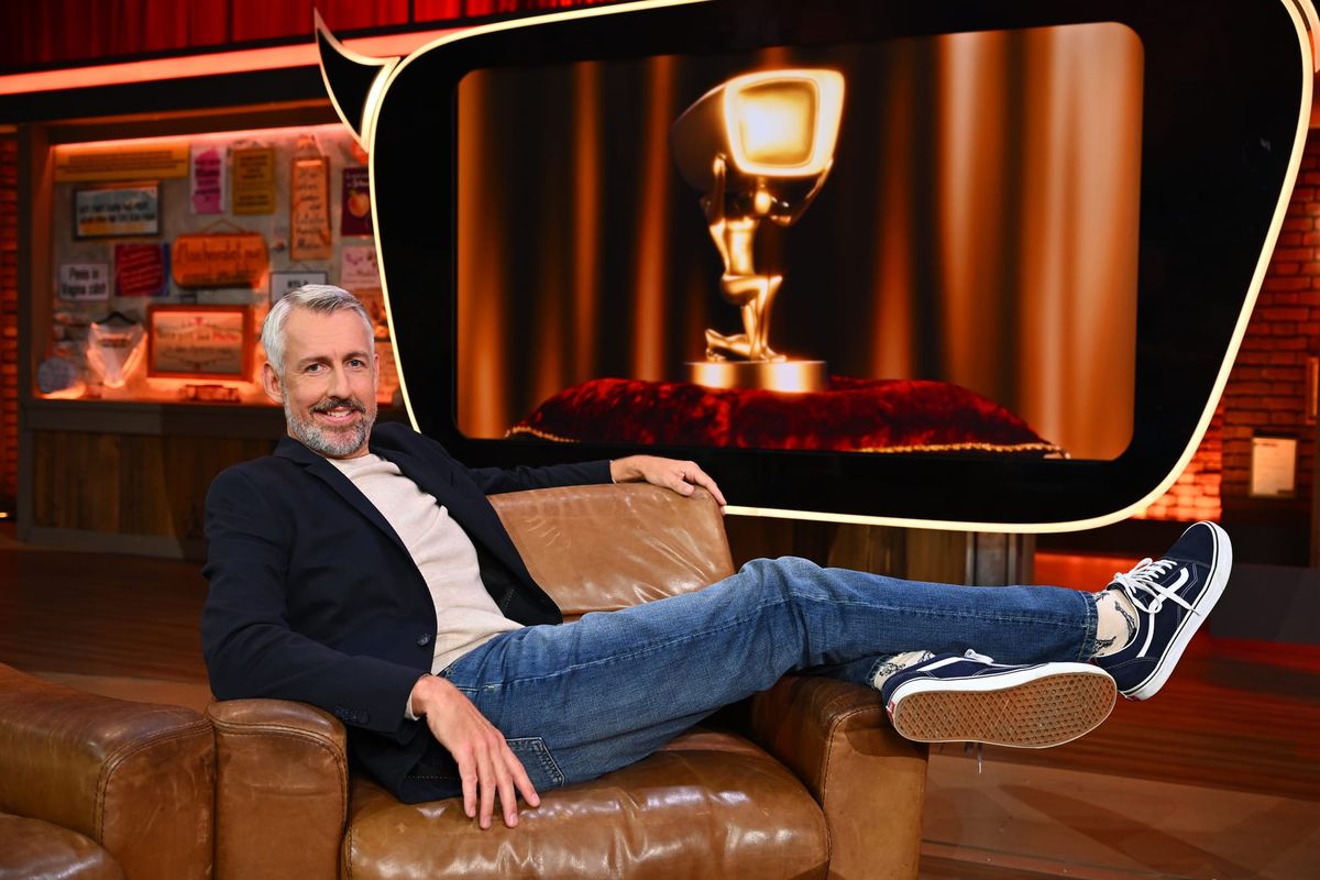 Sebastian Pufpaff lehnt lässig in einem Ledersessel im Studio, im Hintergrund eine Trophäe auf dem Bildschirm