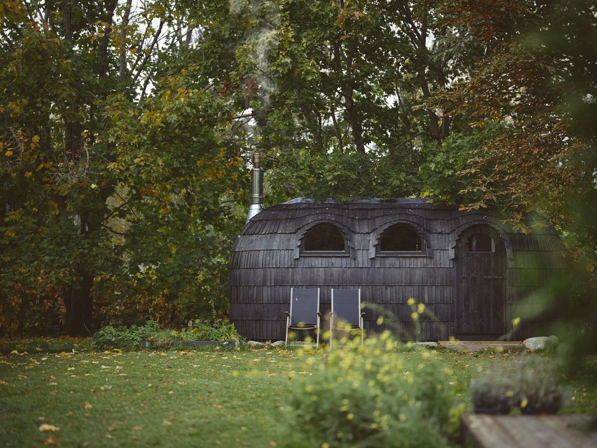 Mit Holzschindeln verkleidete Sauna in Tonnenform im herbstlichen Garten, davor zwei Liegestühle
