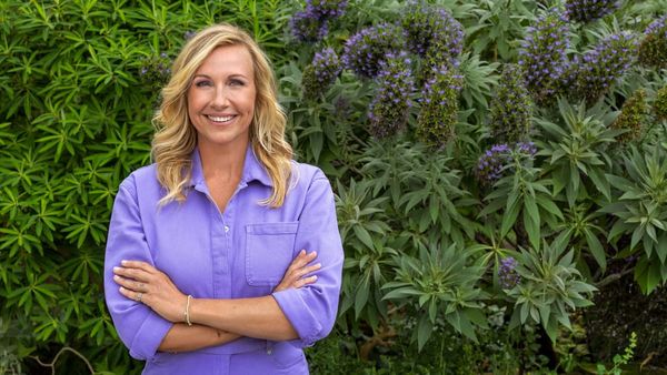 Andrea Kiewel mit verschränkten Armen vor blühenden Sträuchern