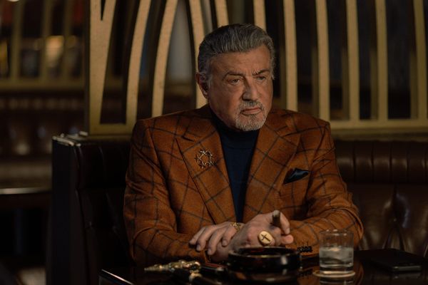 Sylvester Stallone als Dwight Manfredi im karierten Sakko an einem Tisch, Szene aus "Tulsa King"