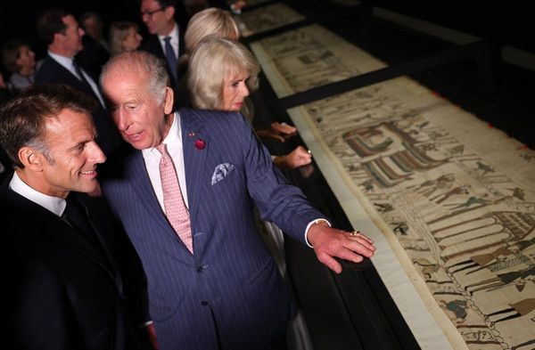 Emmanuel Macron (li.) und König Charles mit ihren Ehefrauen im Hintergrund bei der Besichtigung des Teppichs von Bayeux.