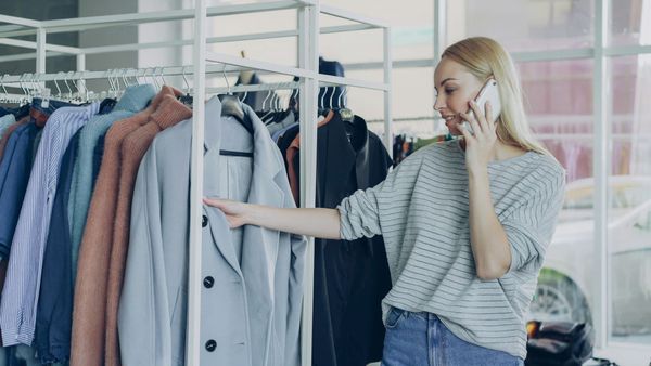 Frau telefoniert und sieht sich Mäntel an einer Kleiderstange an