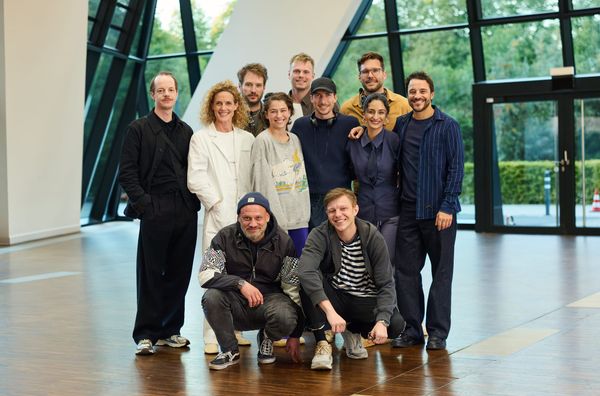 Cast und Team von „A Little Dream of Me“ stehen in einer verglasten Halle zusammen