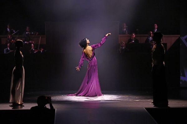 Bühnenszene der ABOUT YOU Fashion Show im Berliner Admiralspalast: Tänzerin im violetten Kleid im Spotlight, dahinter das Orchester