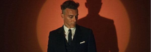 Asaf Avidan im dunklen Anzug vor orangem Spotlicht