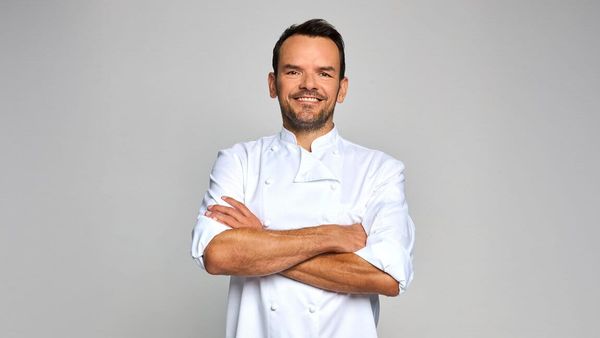 Steffen Henssler in weißer Kochjacke mit verschränkten Armen vor grauem Hintergrund
