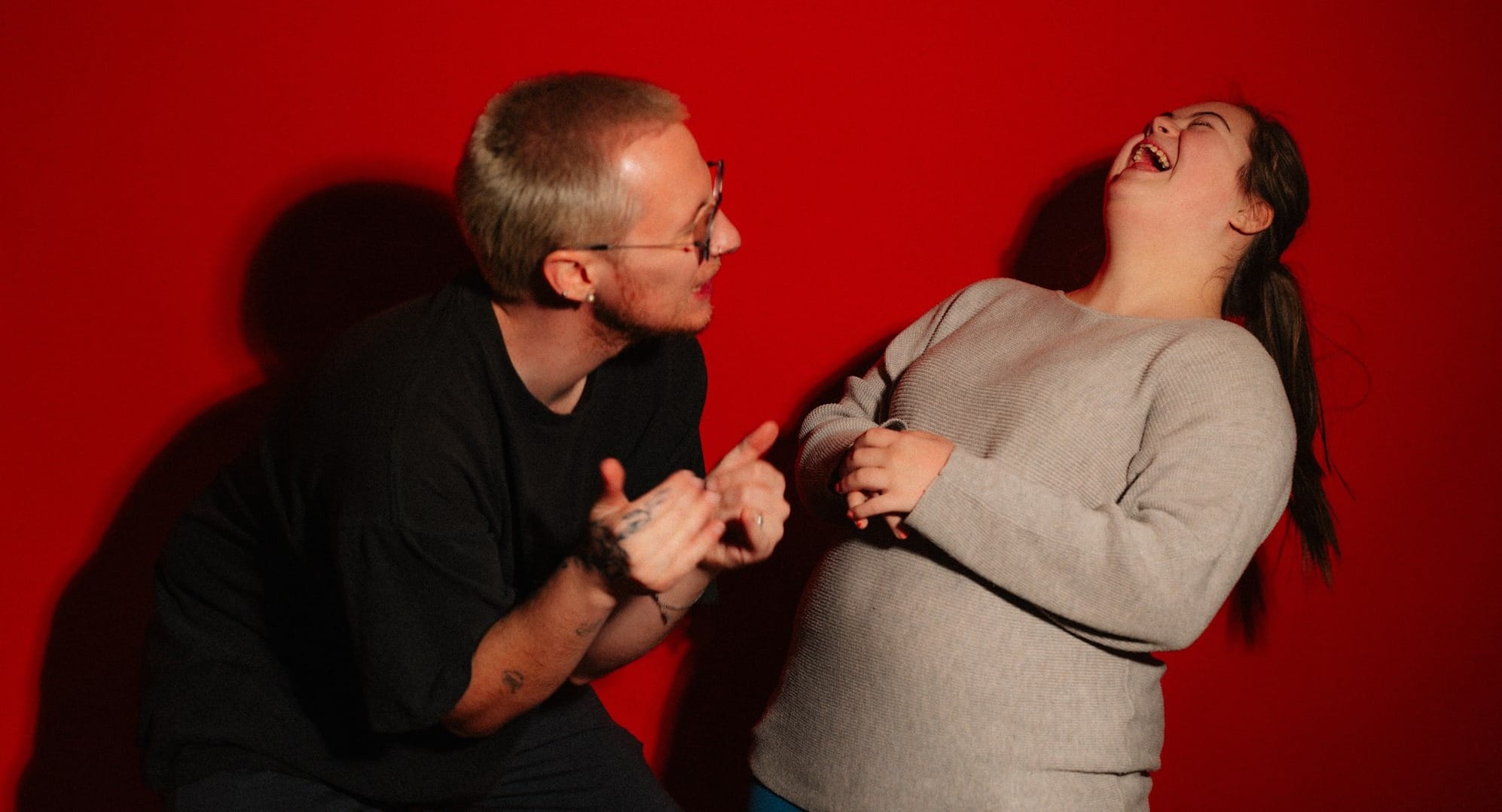 A man and woman laughing against a red background