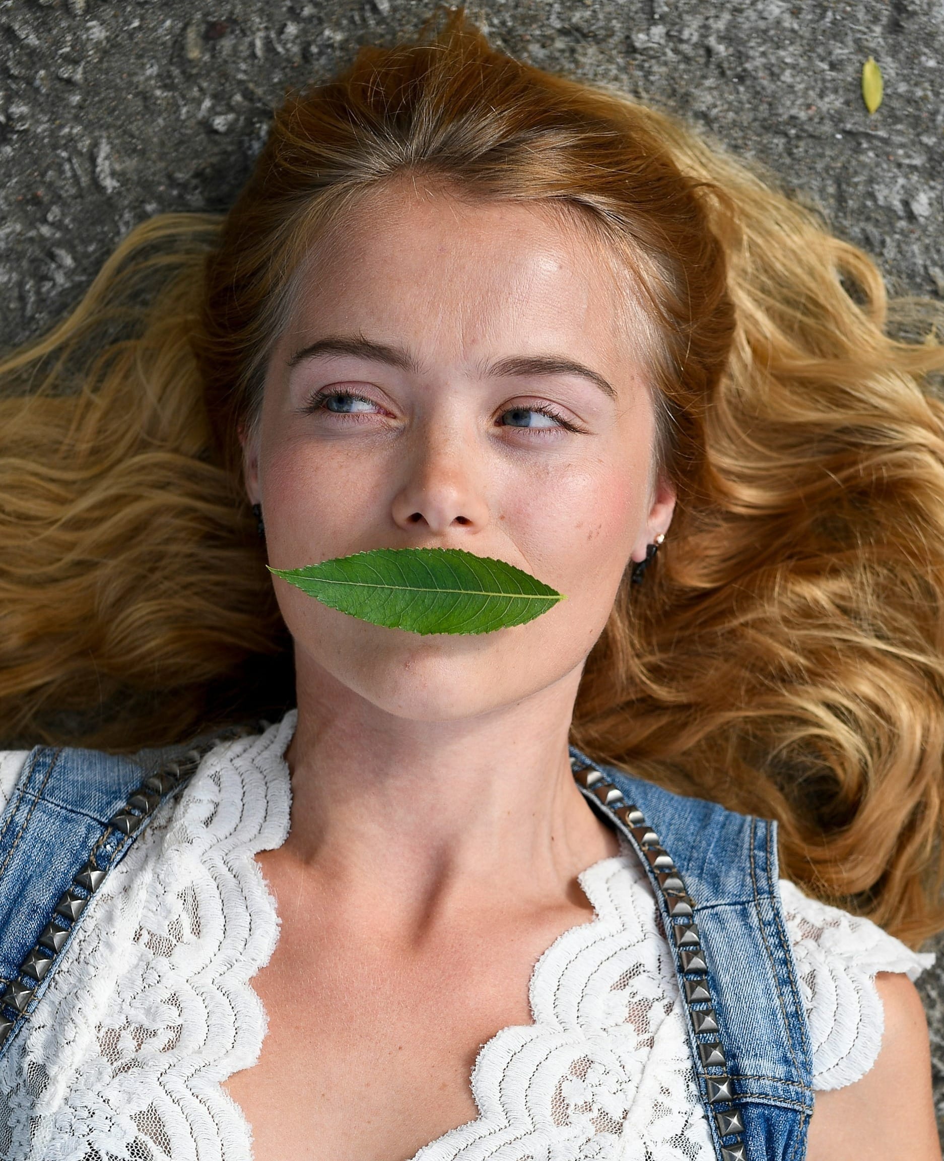 A young woman with a green leaf covering her mouth.