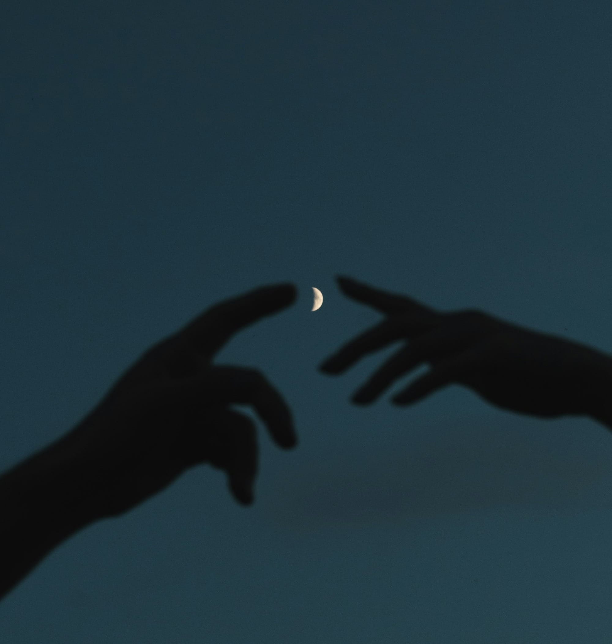 two hands reaching for the moon in the sky