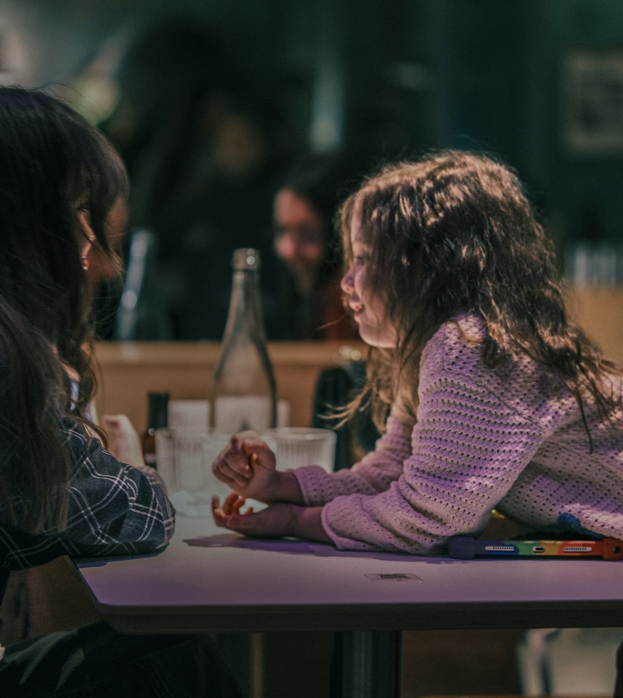 Two girls talking at a table indoors.