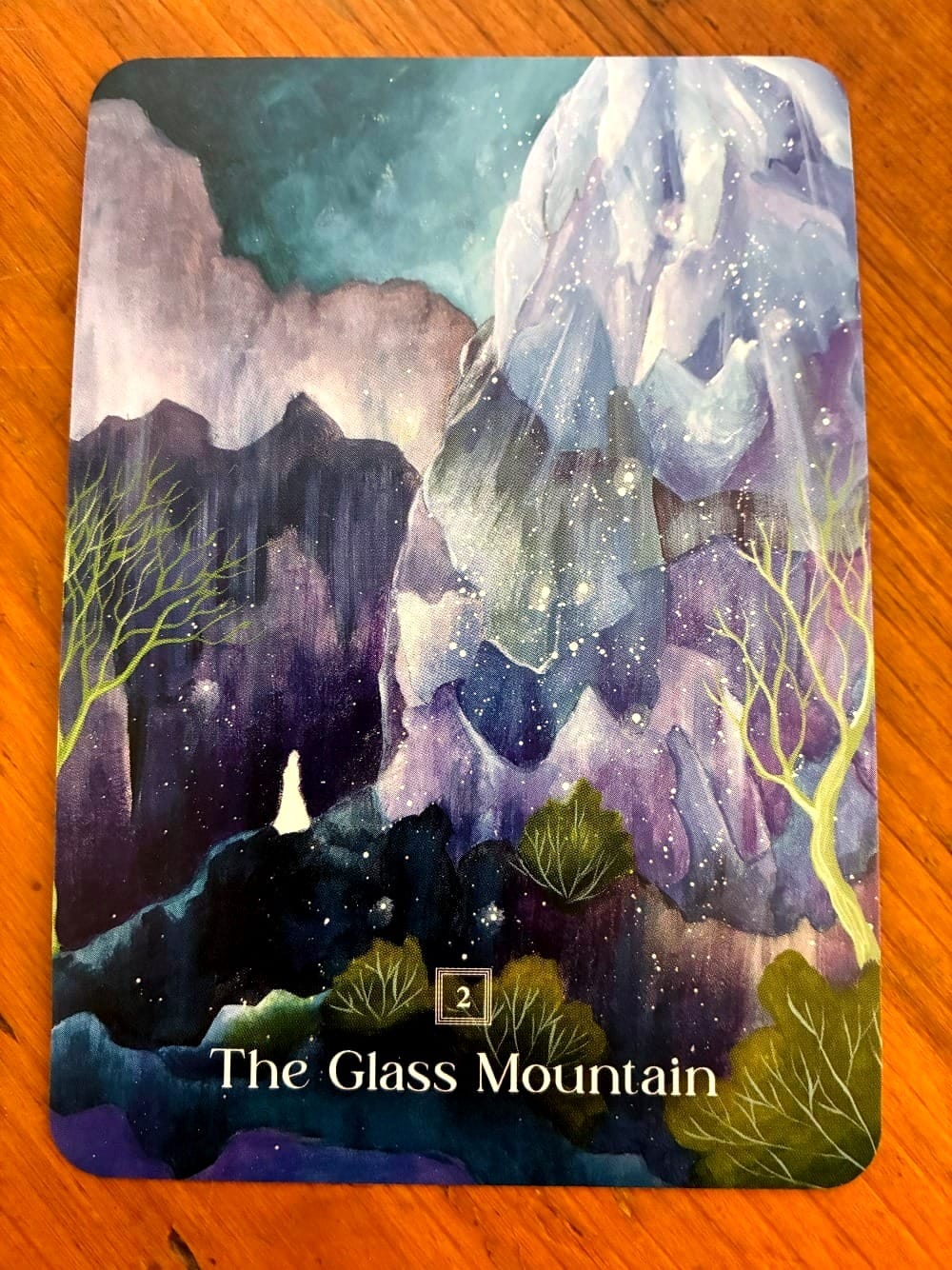 A blue, white and purple mountain range, with trees near the bottom.