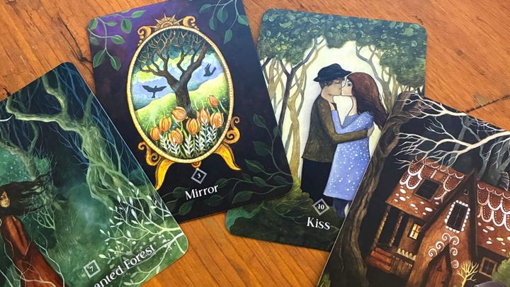 Four Tarot cards spread out on a table: the enchanted forest, the mirror, the kiss, the witch's cottage.