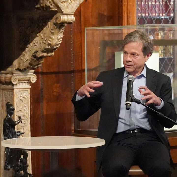 Two men speak into microphones with a short round table in between them. 