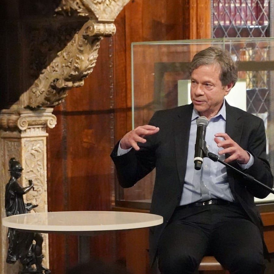 Two men speak into microphones with a short round table in between them. 