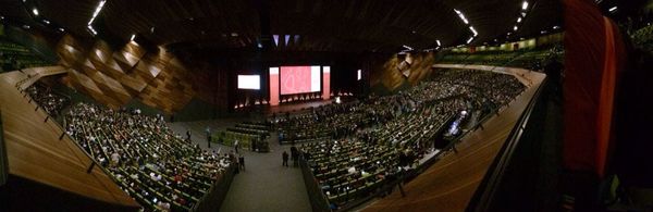 A slightly fish-eye-distorted view of a huge audience at a conference, taken from the back of the auditorium.