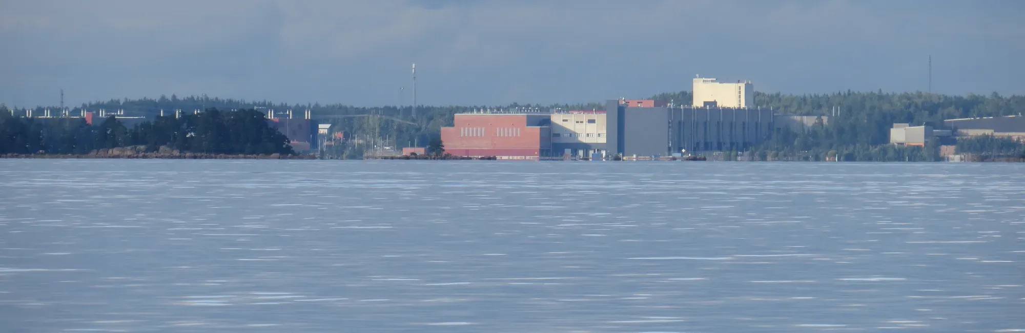 Googles datacenter i Fredrikshamn sett från Finska viken, industribyggnader vid strandlinjen med skog bakom