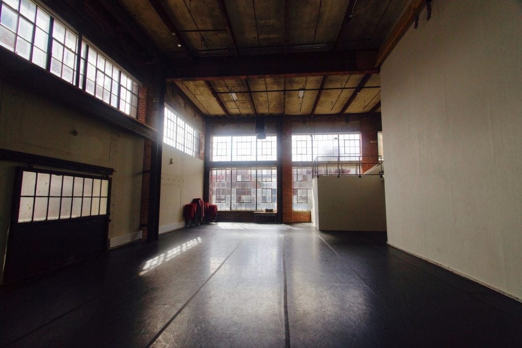 Sunlight streams into a wide-open dance studio space, bouncing off the black marley.