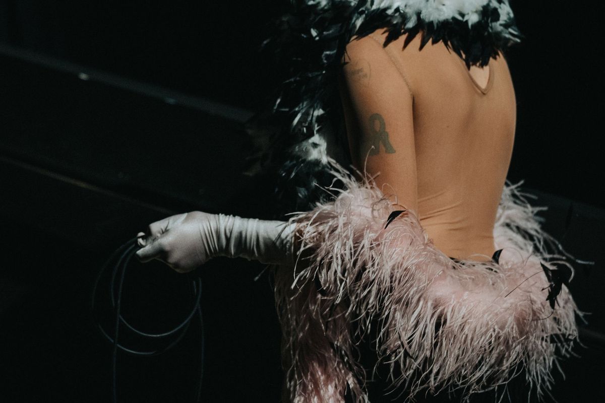 A performer wearing several feather boas with black, white, and pink feathers stands with her back to the camera.