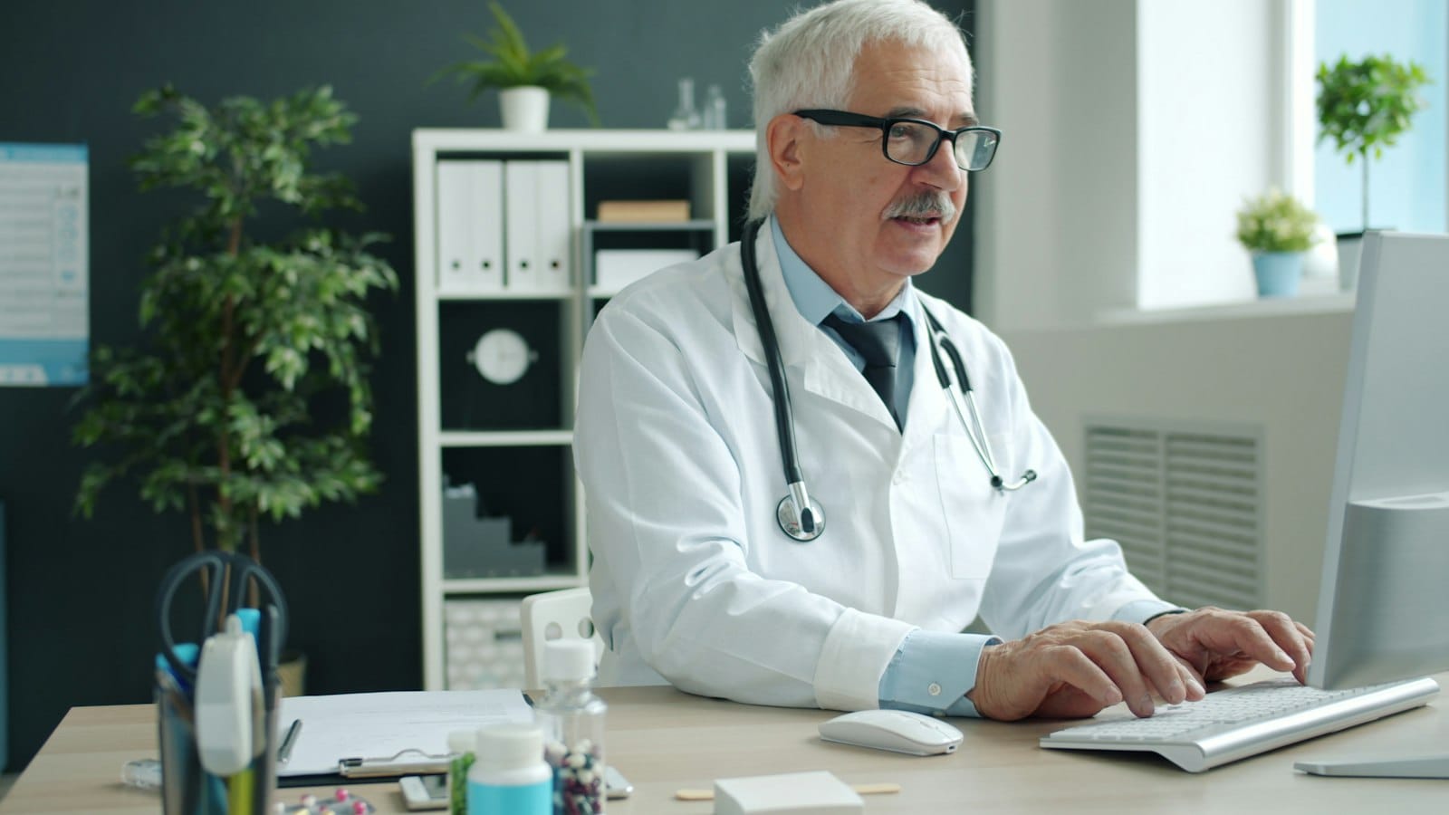 A clinician typing at a desktop computer in a consulting room