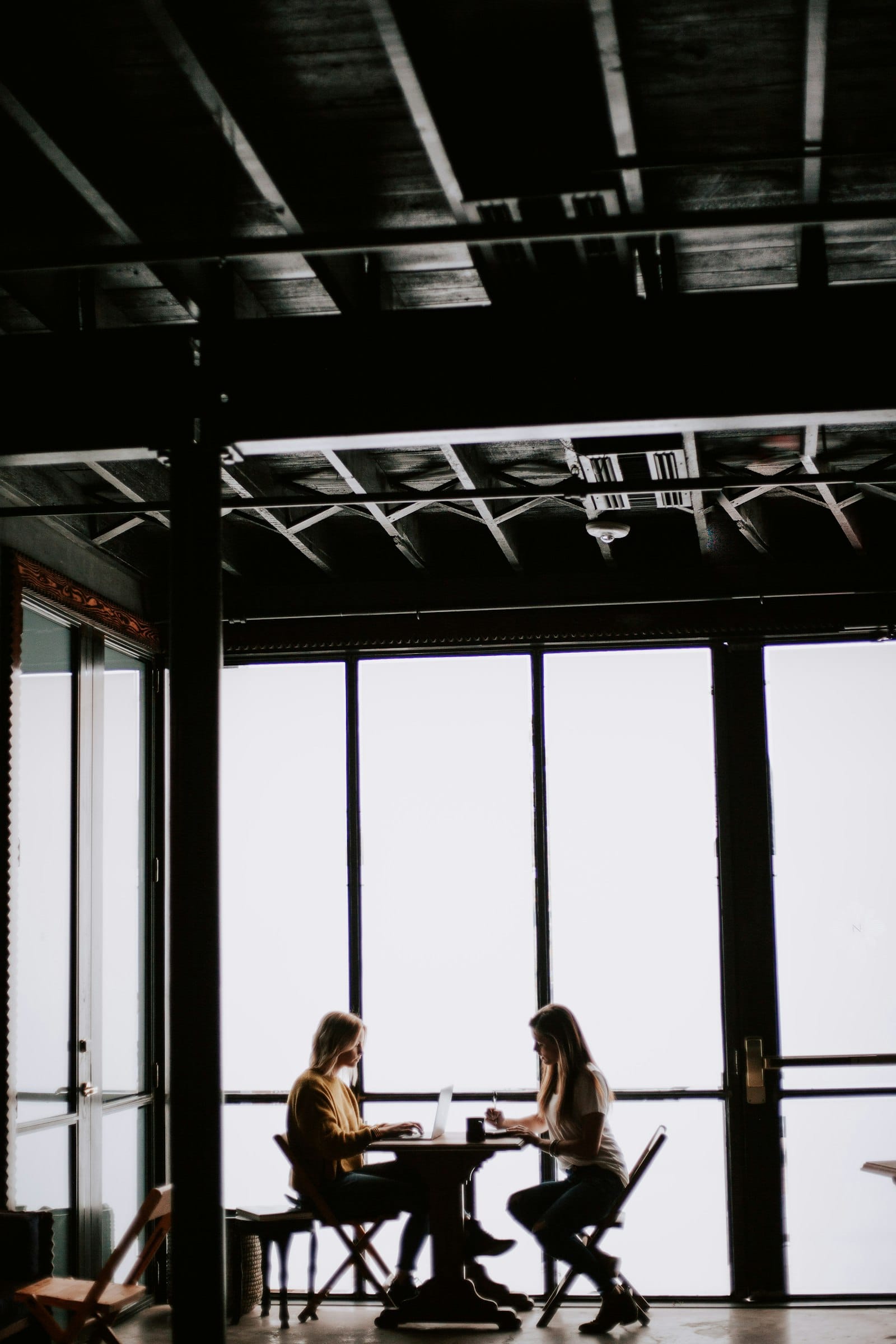 Two people sitting facing each other at a small table in a large empty room