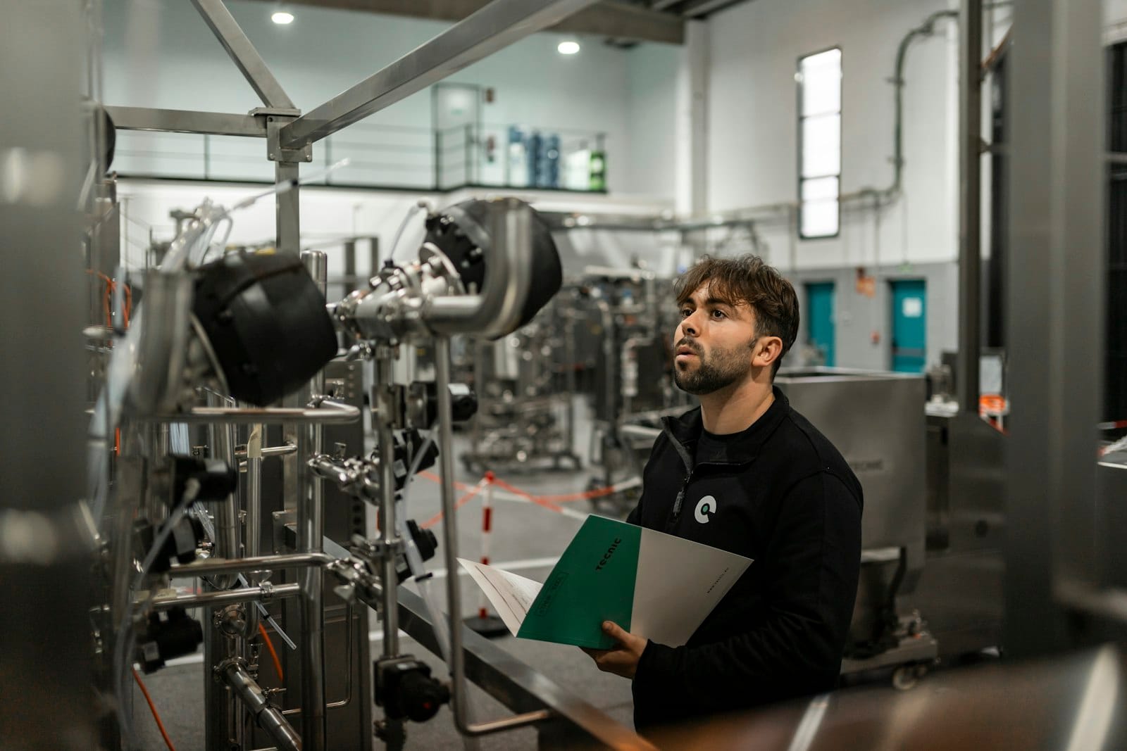 A technician in a validation room holding technical documentation while checking an industrial piping installation